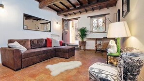 A cozy living room with a brown sectional sofa, a white fur rug, and a wooden ceiling. - San Callisto - WR Apartments (Rome)
