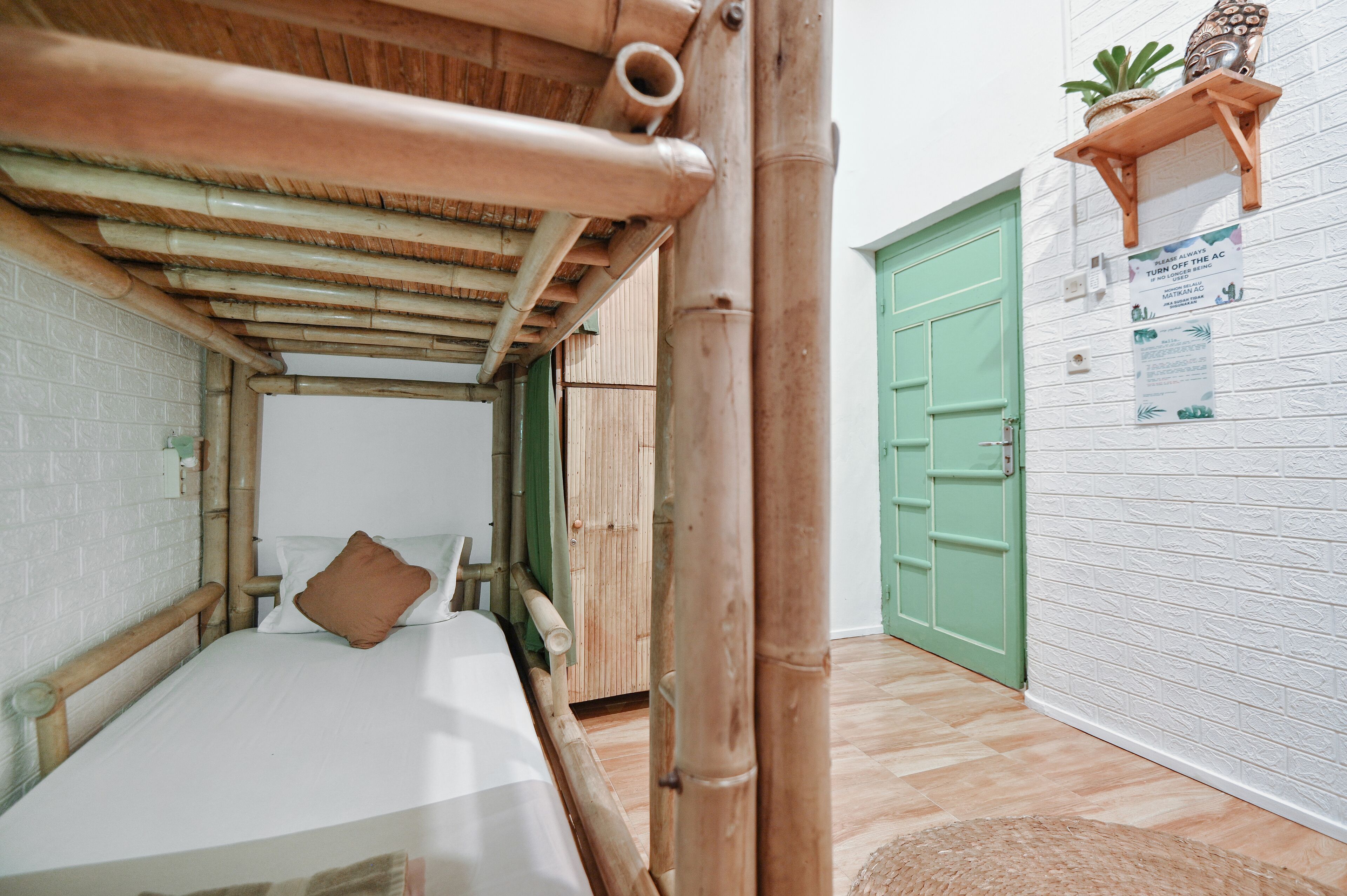A room with a bed, bamboo ceiling, green door, and a small shelf with a plant.