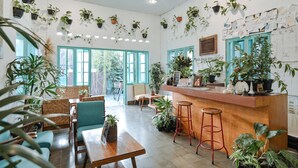 A cozy cafe with wooden furniture, a bar area, and numerous potted plants. - Snooze Guesthouse Yogyakarta - Hostel (Yogyakarta)