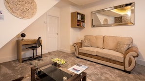 A living room with a beige sofa, a glass coffee table, a wooden desk with a chair, a bookshelf, and a large mirror on the wall. - Landmark Apartments Harrogate (Harrogate)