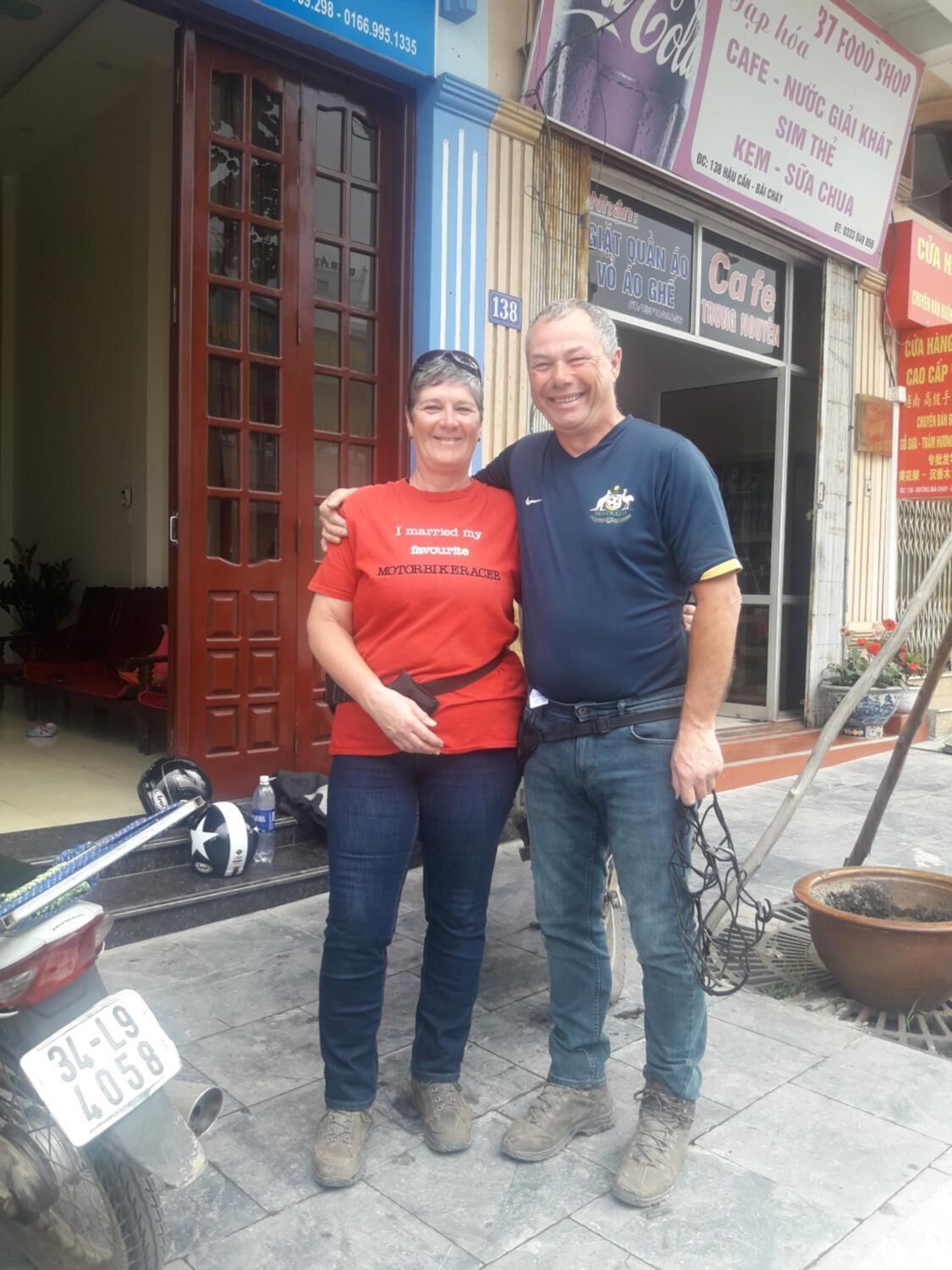 A couple standing in front of a cafe with a signboard.