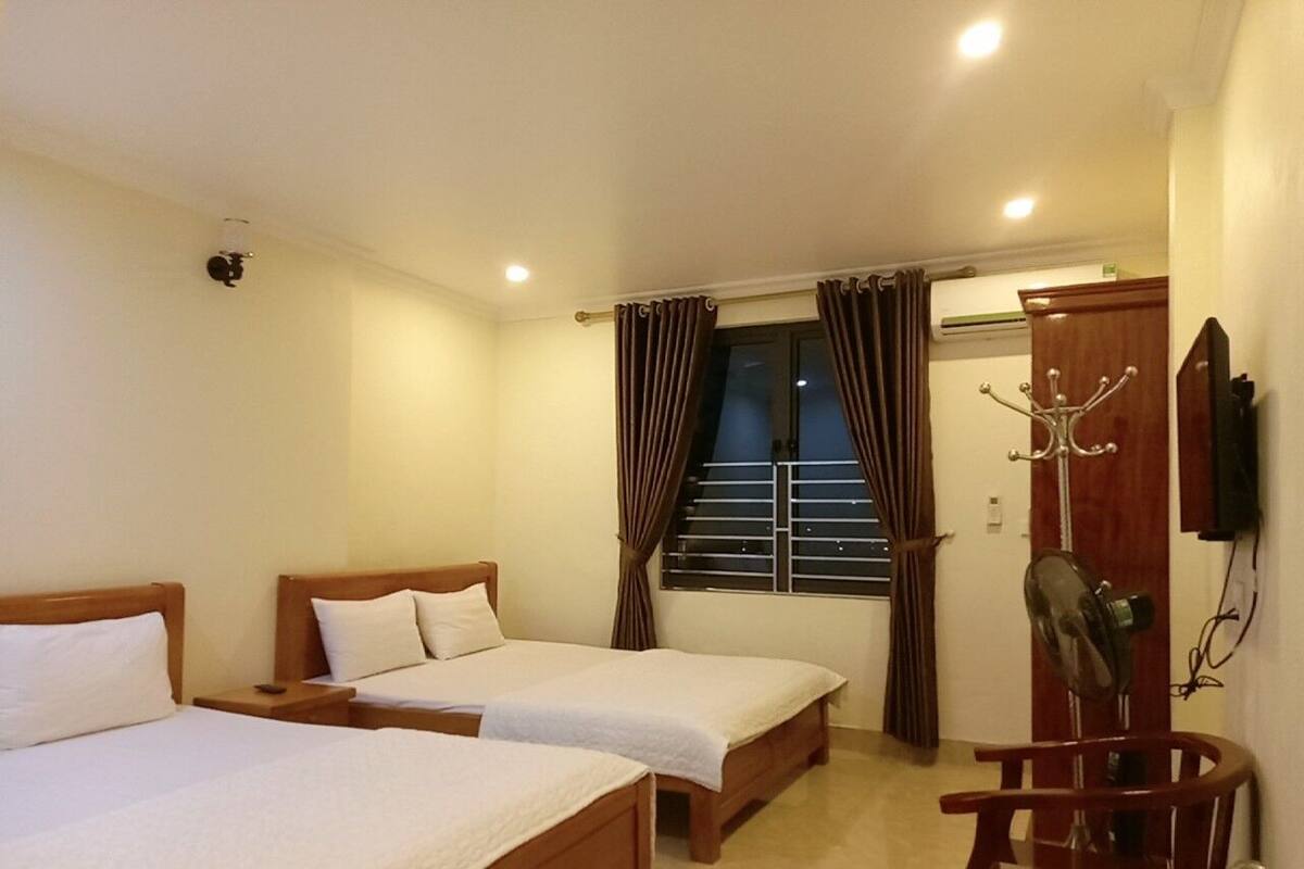 A hotel room with two single beds, a wooden chair, a coat rack, and a television mounted on the wall.
