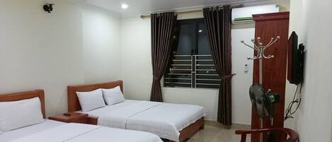 A hotel room with two single beds, a wooden wardrobe, a coat rack, and a small table.