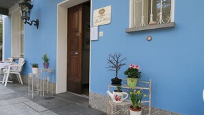 A blue building with a wooden door, a sign for Albero Bar, and potted plants on metal stands. - Piccolo Hotel (Muralto)