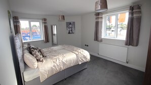 Een slaapkamer met een bed, een raam met gordijnen, een radiator en een foto aan de muur.