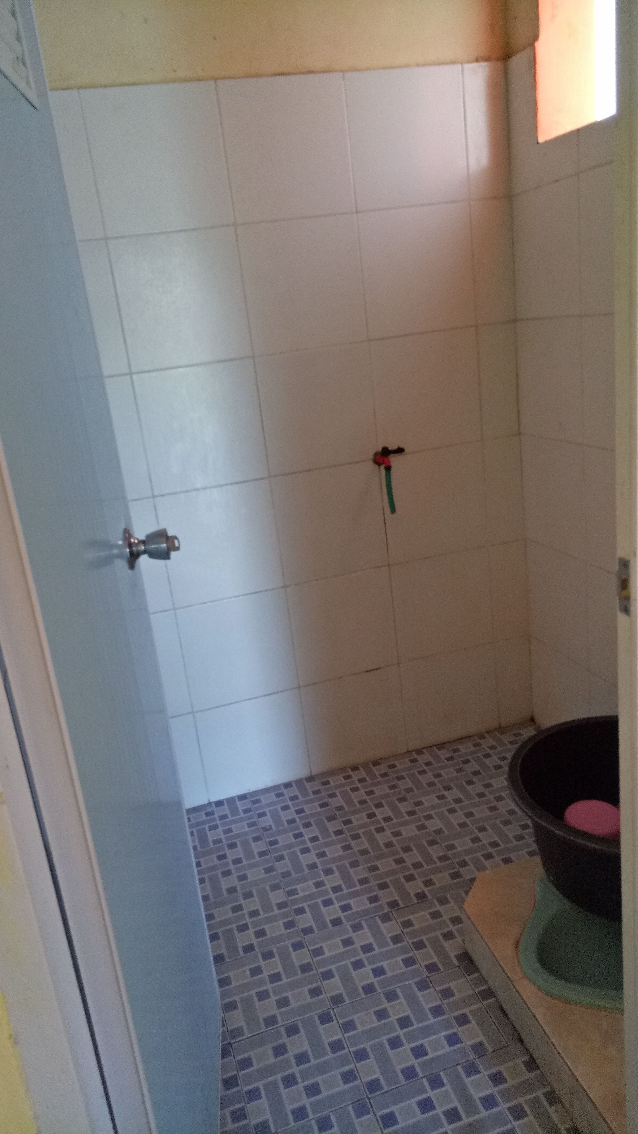 A bathroom with white tiled walls, a blue and gray patterned floor, a black bathtub, and a green showerhead.