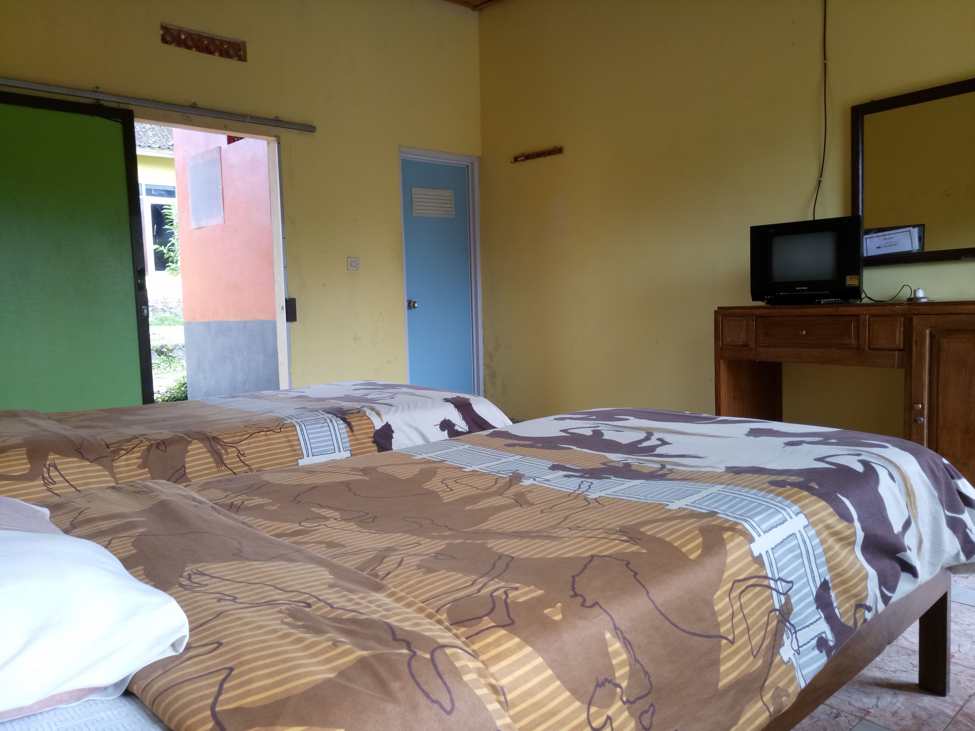 Una habitación con dos camas, un televisor sobre un mueble de madera y una puerta que da al exterior.