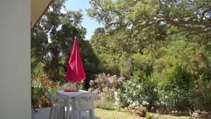 Un patio con mesa y sillas, rodeado de un jardín con diversas plantas y flores.