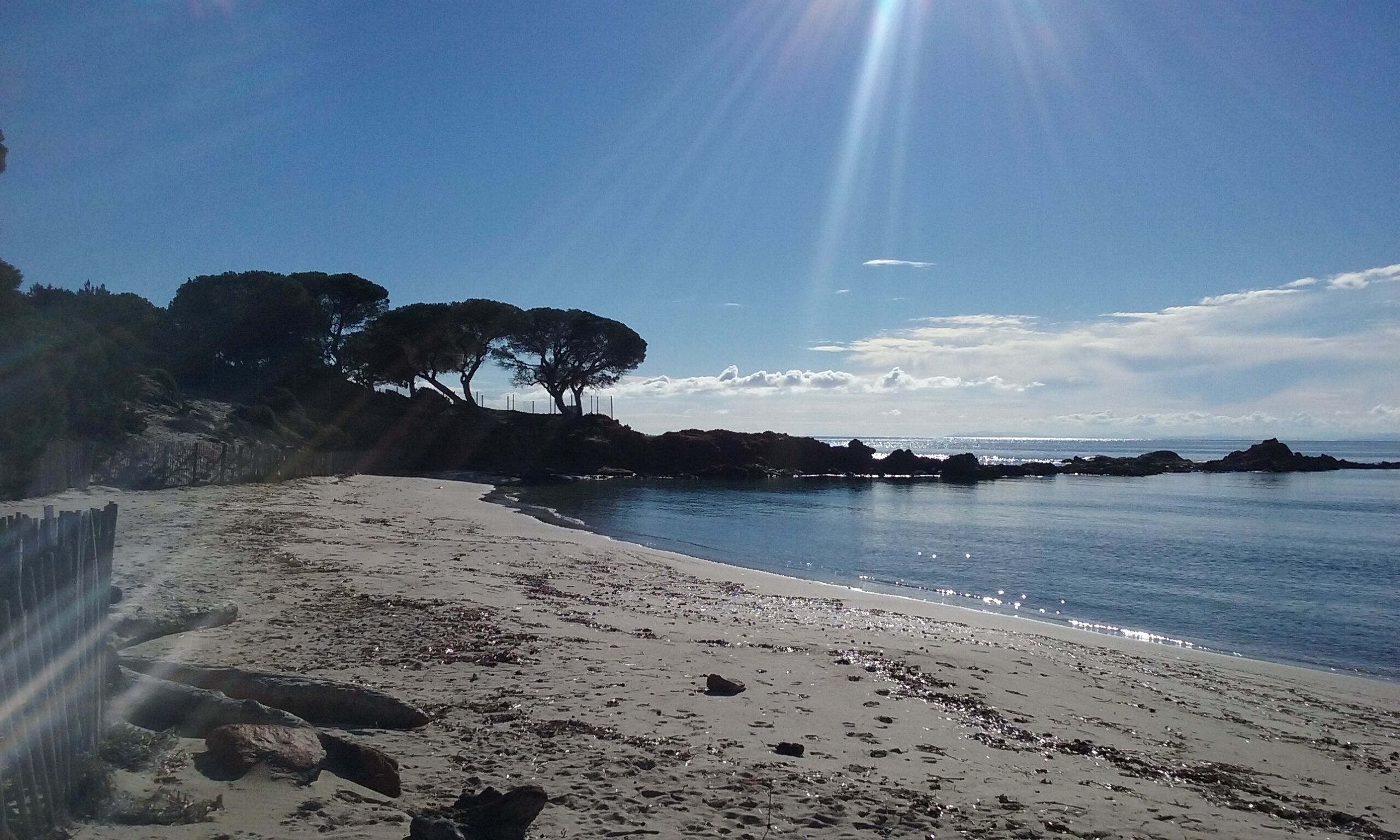 A beach with white sand, rocky outcrops, and trees.
