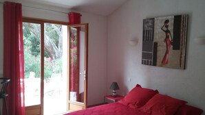 Un dormitorio con cama, mesita de noche, lámpara, un cuadro y un ventanal corredera que da a un balcón.
