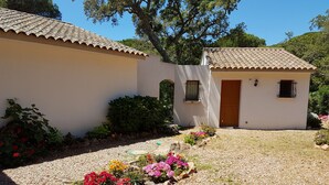 Un edificio de dos pisos con techo de tejas, un pequeño jardín con flores coloridas y un camino de entrada de grava.