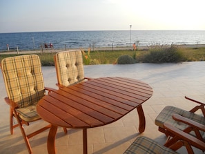 A wooden table and two chairs with plaid cushions, set on a patio with a view of the sea. - Apartments Alen (Umag)