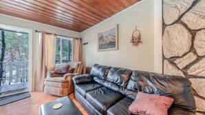 A cozy living room with a leather sofa, a cushioned chair, and a stone accent wall.