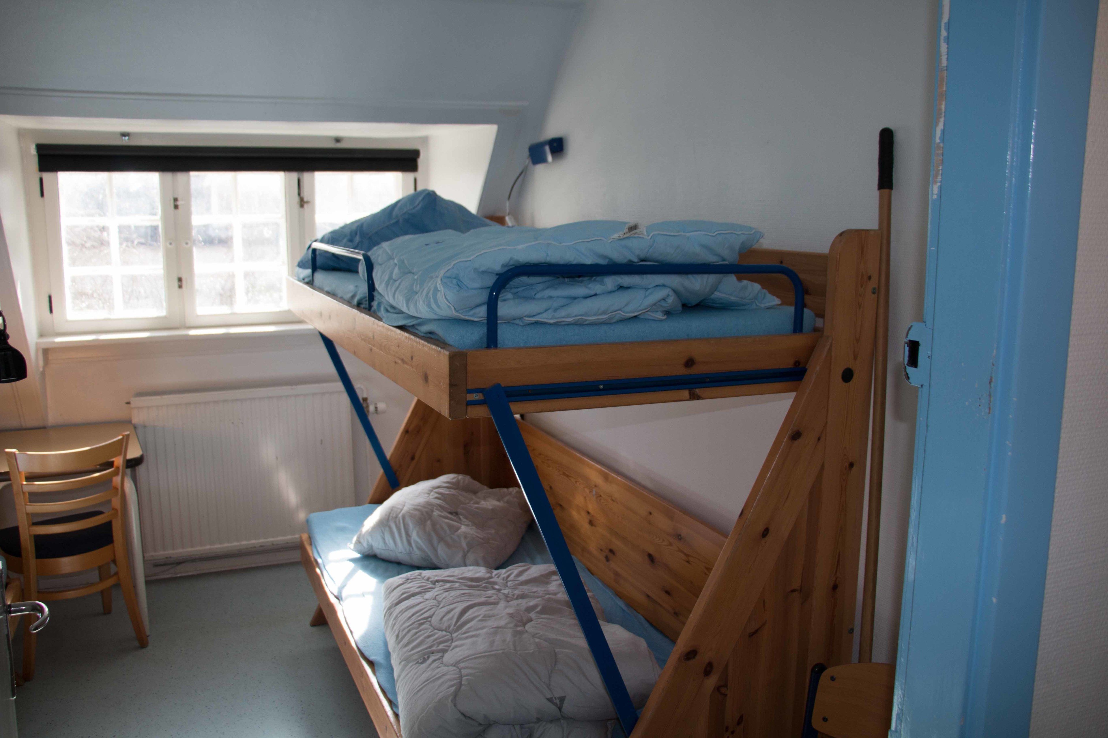 A dormitory room with bunk beds, a desk, and a chair.
