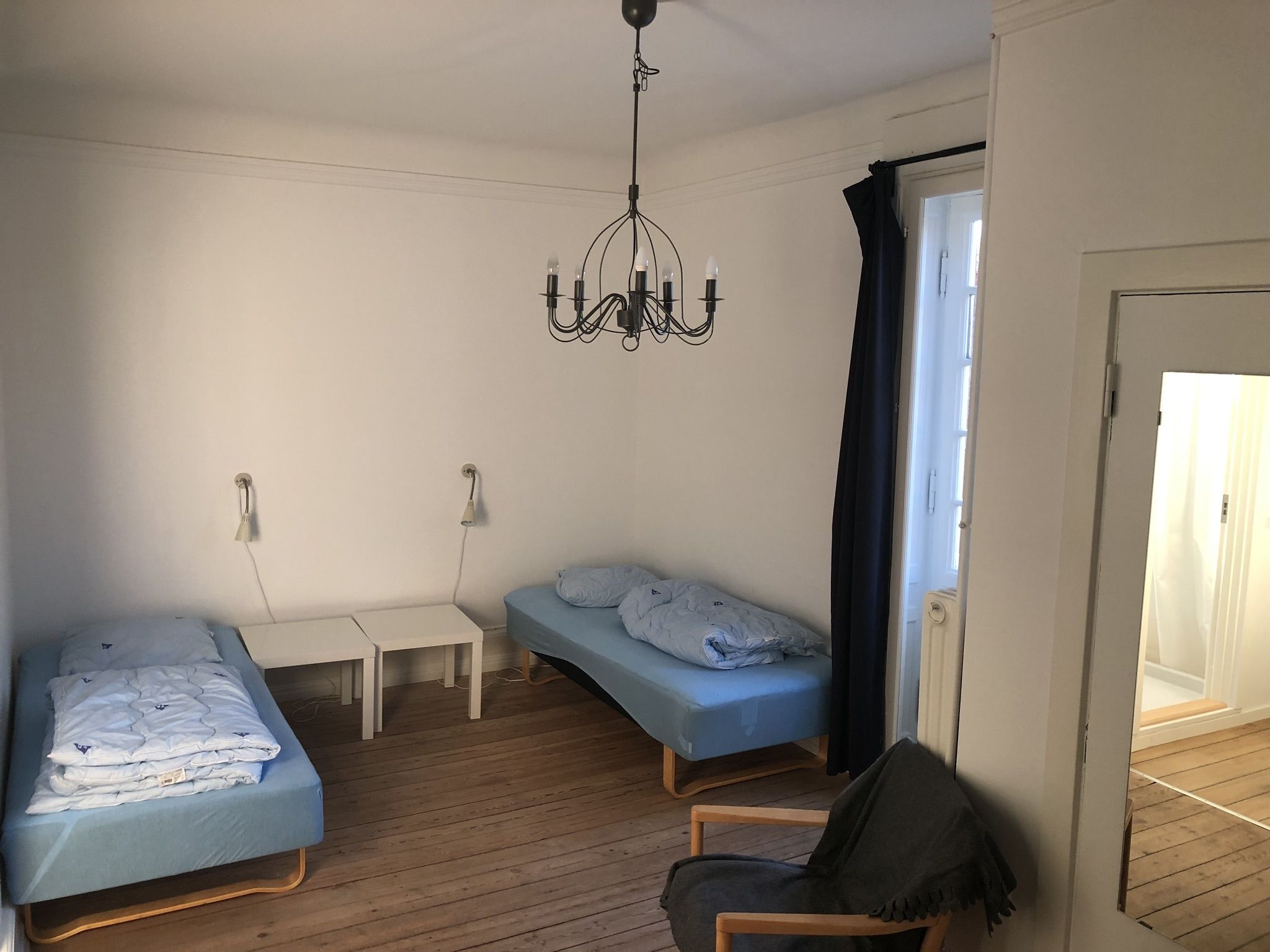 Una habitación con dos camas individuales, una mesita, una silla y una araña.