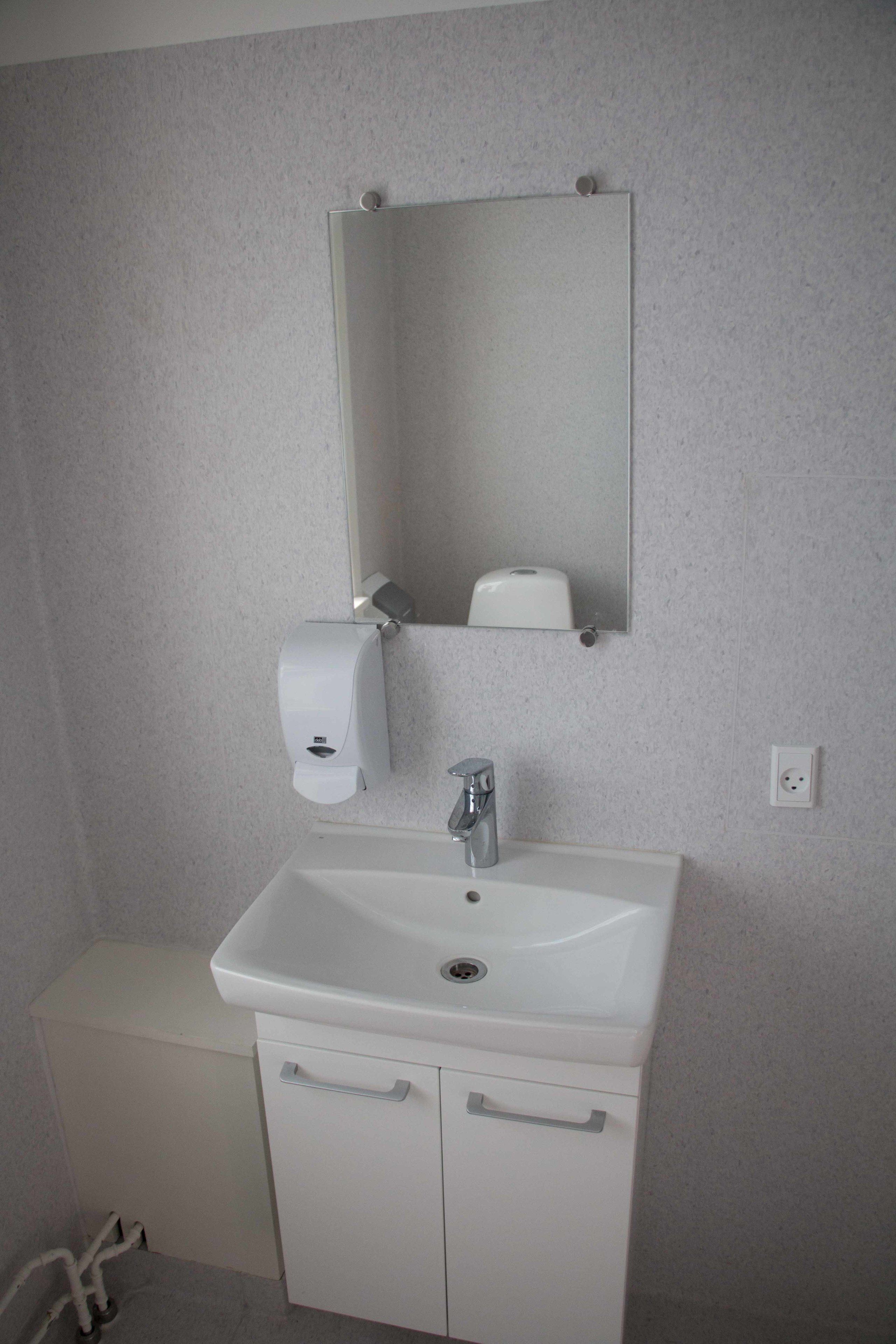 Une salle de bain avec un lavabo blanc, un miroir et un distributeur de serviettes en papier.