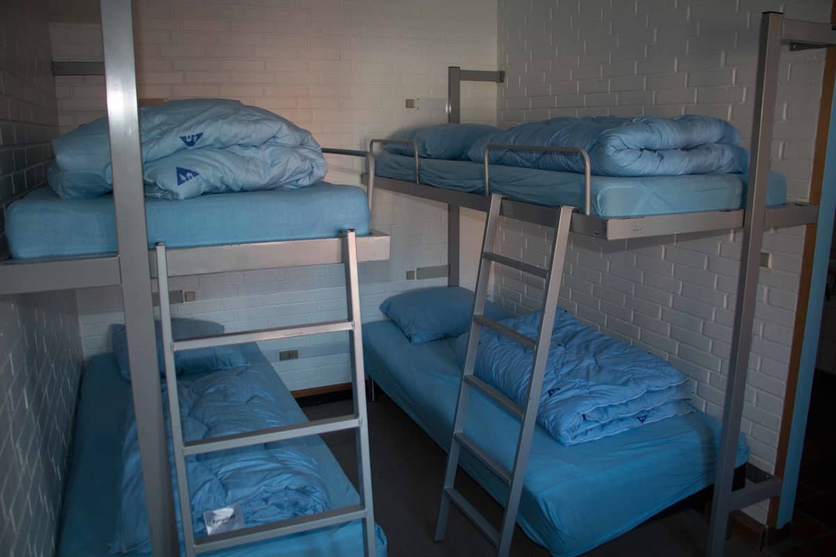 Etagenbetten mit blauer Bettwäsche, weißen Ziegelwänden und Metallgeländern.