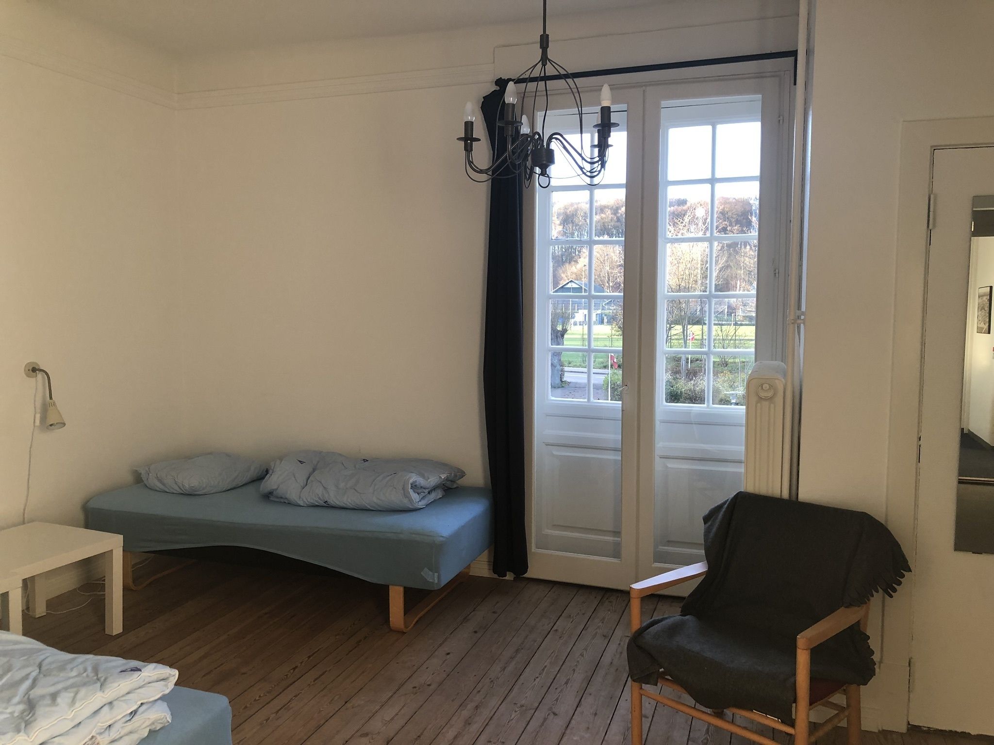 A room with a bed, a chair, a table, and a window with a view of trees.