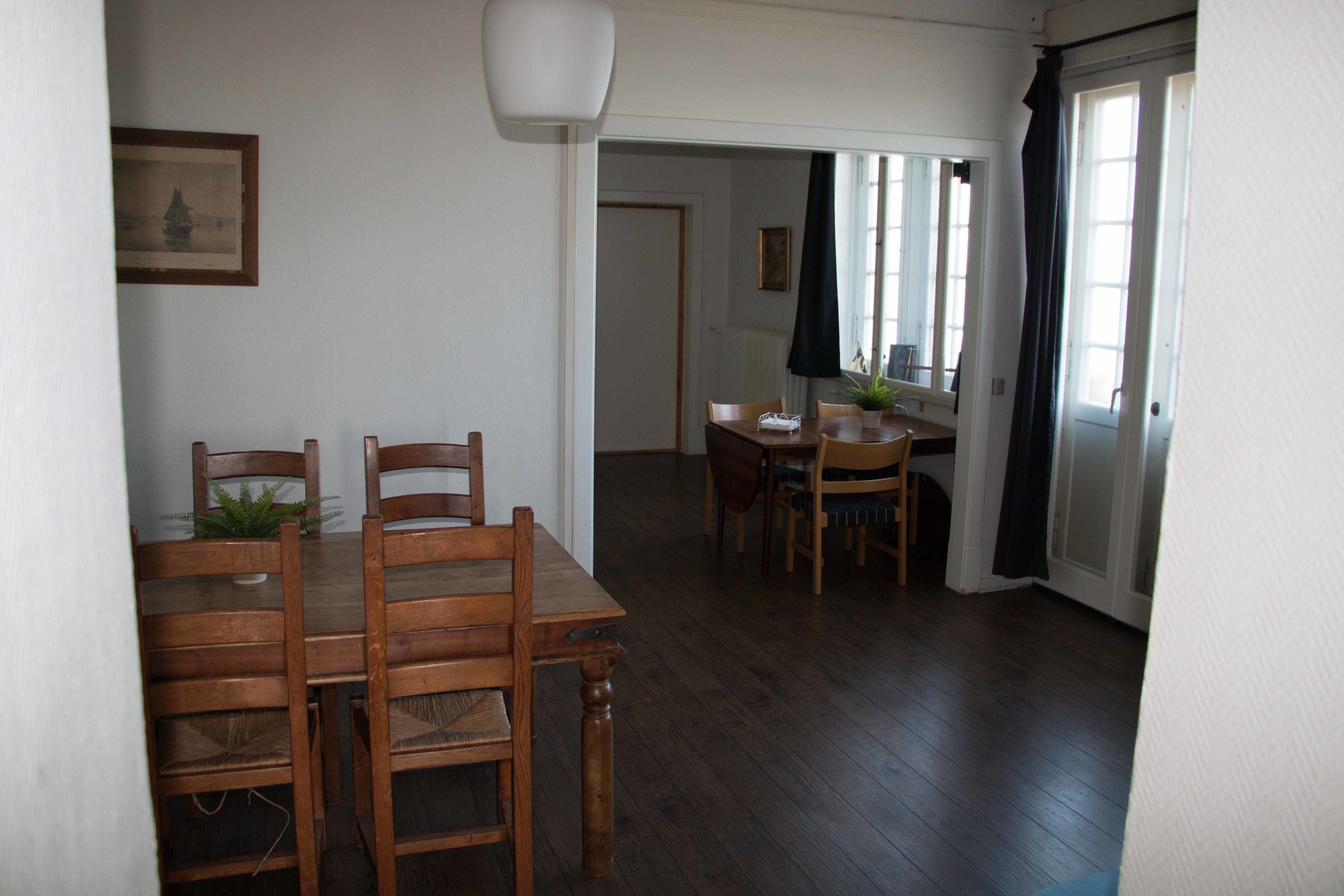 A dining area with wooden tables and chairs, a potted plant, and a framed picture on the wall.