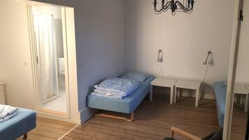 A small, well-lit room with a bed, a chair, a desk, and a chandelier.