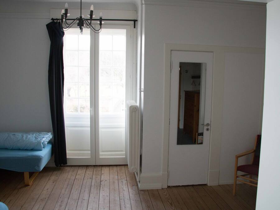 Ein Zimmer mit einem Bett, einem Sessel, einer Tür und einem fensterbepflegten Fenster.
