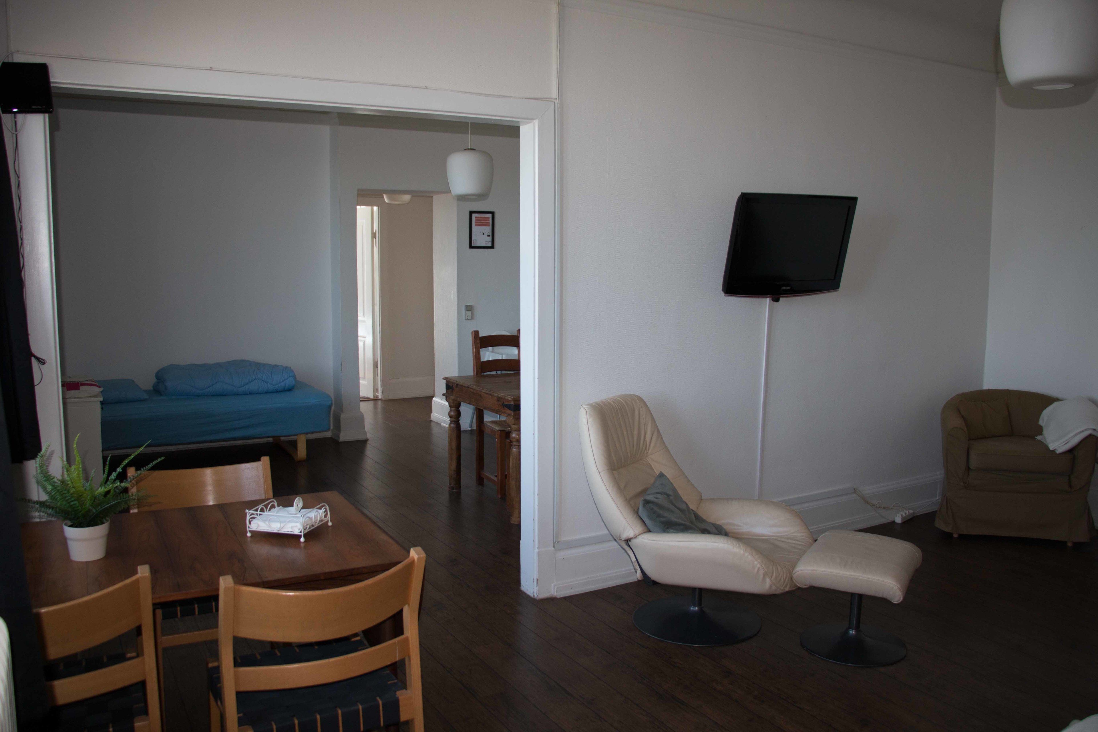 A living room with a TV, a sofa, a dining table with chairs, and a chair with a pillow.