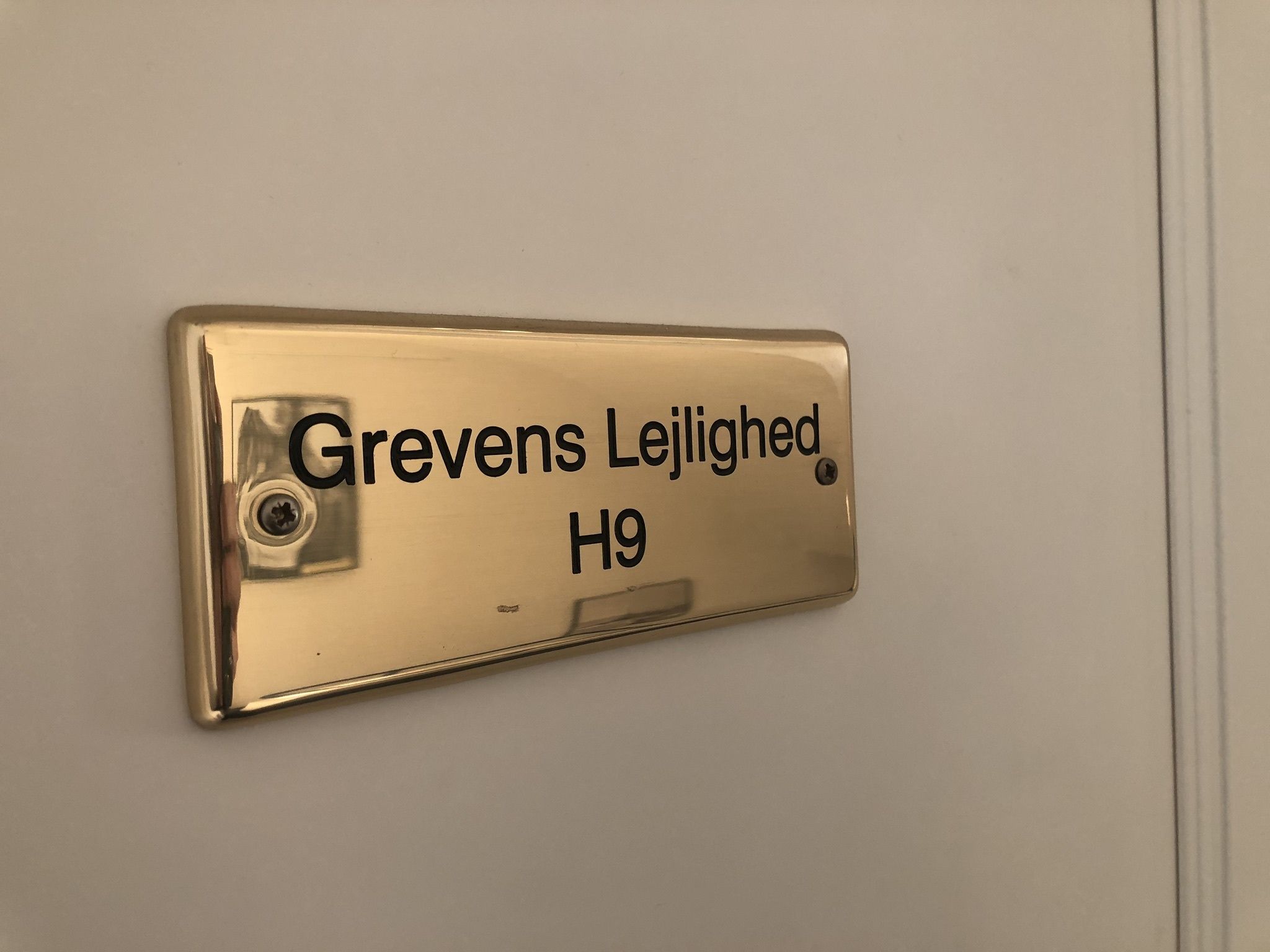 Placa dorada con el texto 'Grevens Lejlighed H9' montada en una pared.