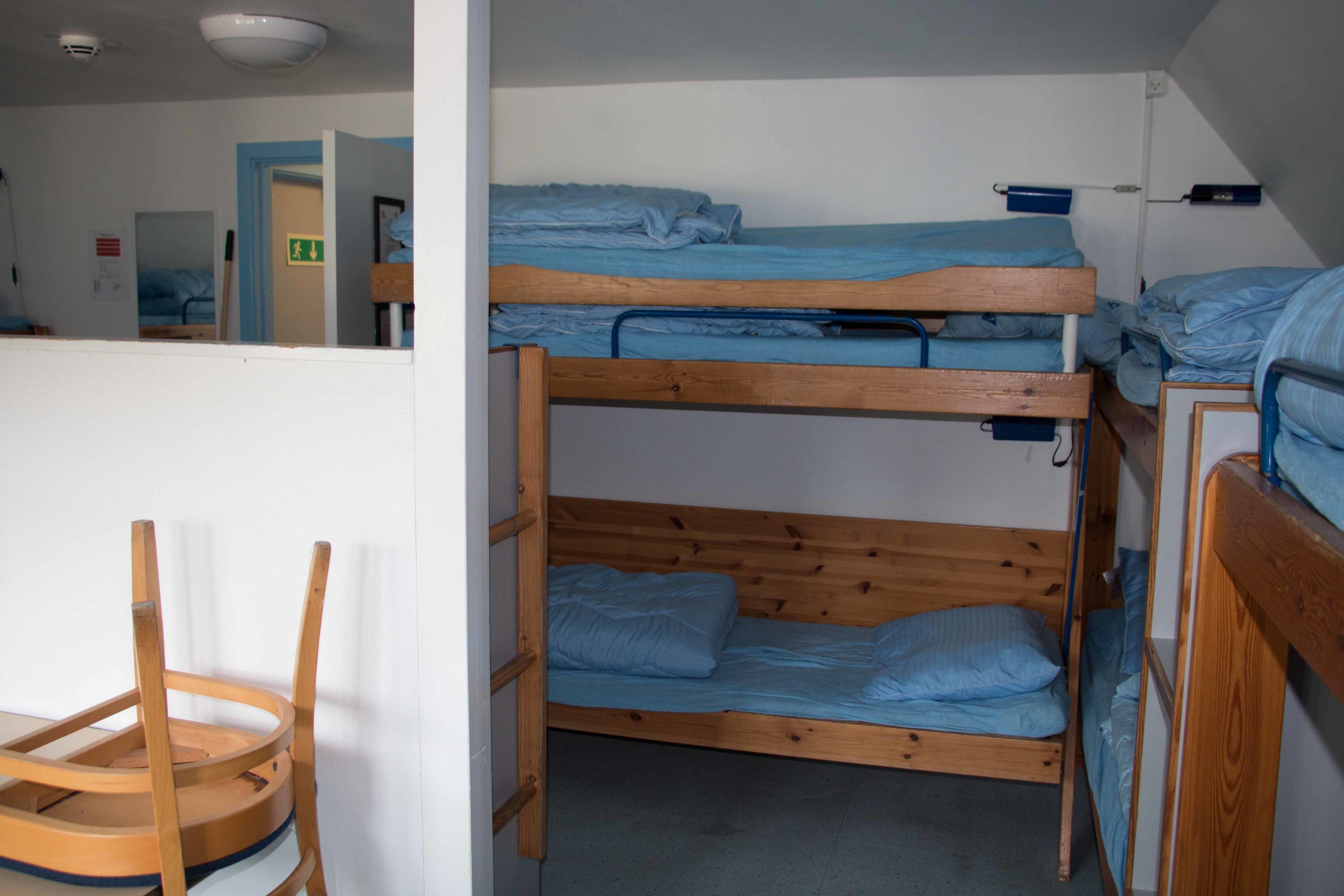 Un dormitori amb llits superposats, una cadira de fusta i una porta oberta que dona a una altra habitació.