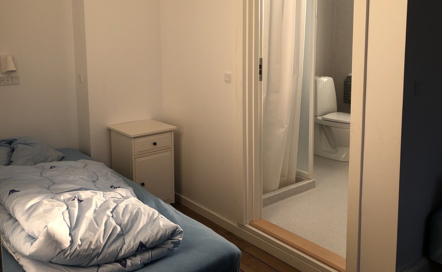 Un dormitorio con cama, mesita de noche y vistas a un baño a través de una puerta.
