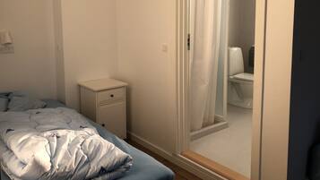Un dormitorio con cama, mesita de noche y vistas a un baño a través de una puerta.