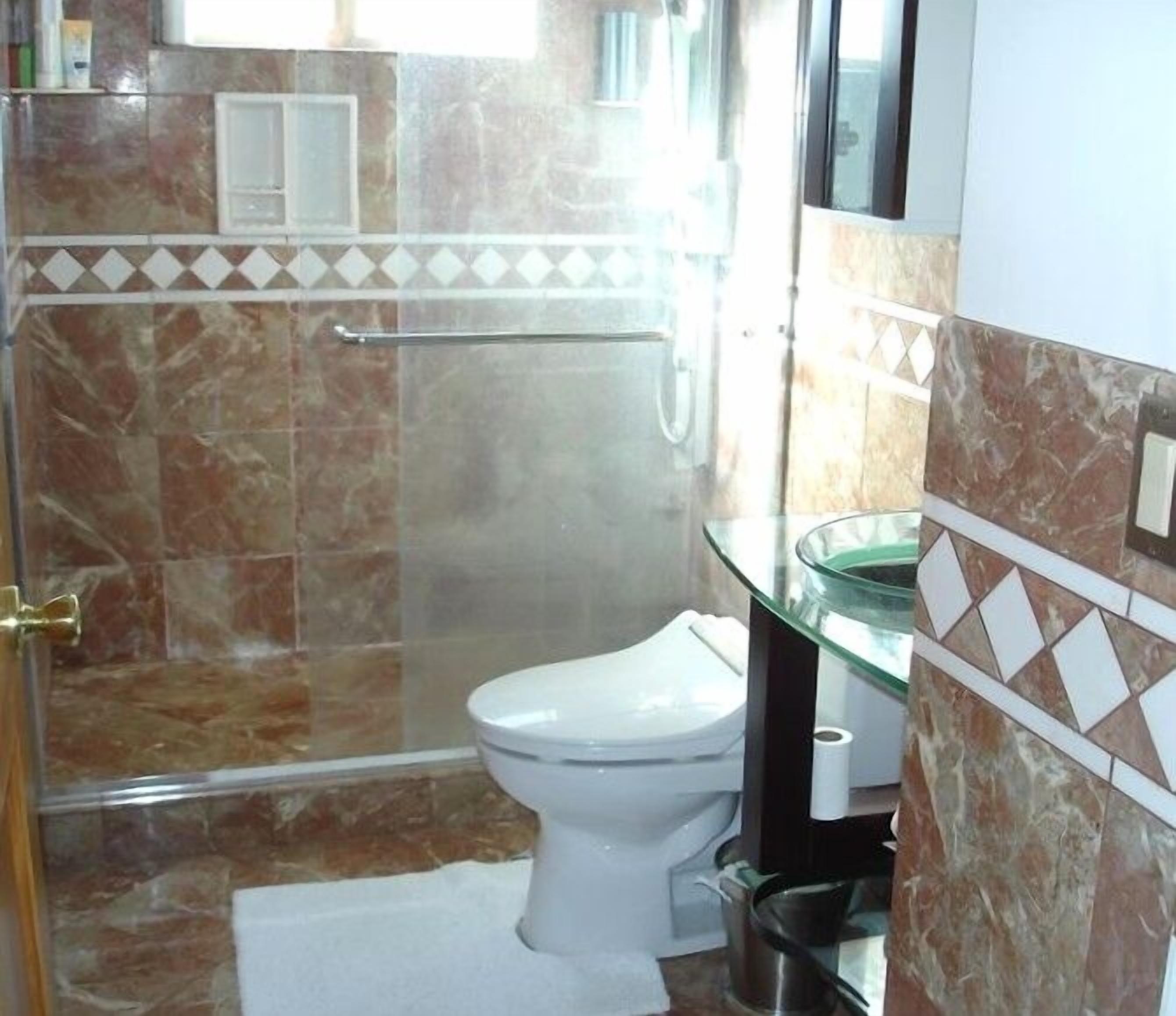 Casa de banho com cabine de chuveiro em vidro, sanita e lavatório de vidro.