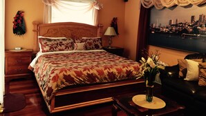 A bedroom with a large bed, a nightstand, a bedside table with a lamp, a vase with flowers, and a cityscape view through a window. - Comfortable Vacation Home Near ~SFO~ Airport (San Bruno)