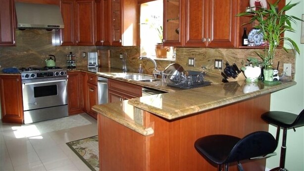 A kitchen with wooden cabinets, a granite countertop, stainless steel appliances, and a bar area. - Comfortable Vacation Home Near ~SFO~ Airport (San Bruno)