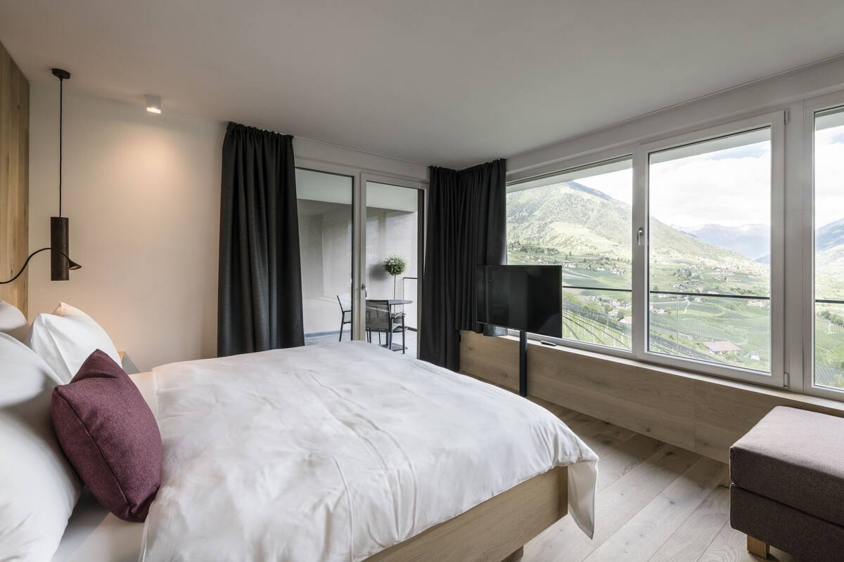 Une chambre d’hôtel moderne dotée d’un grand lit, d’une télévision et d’un balcon offrant une vue panoramique sur les montagnes.