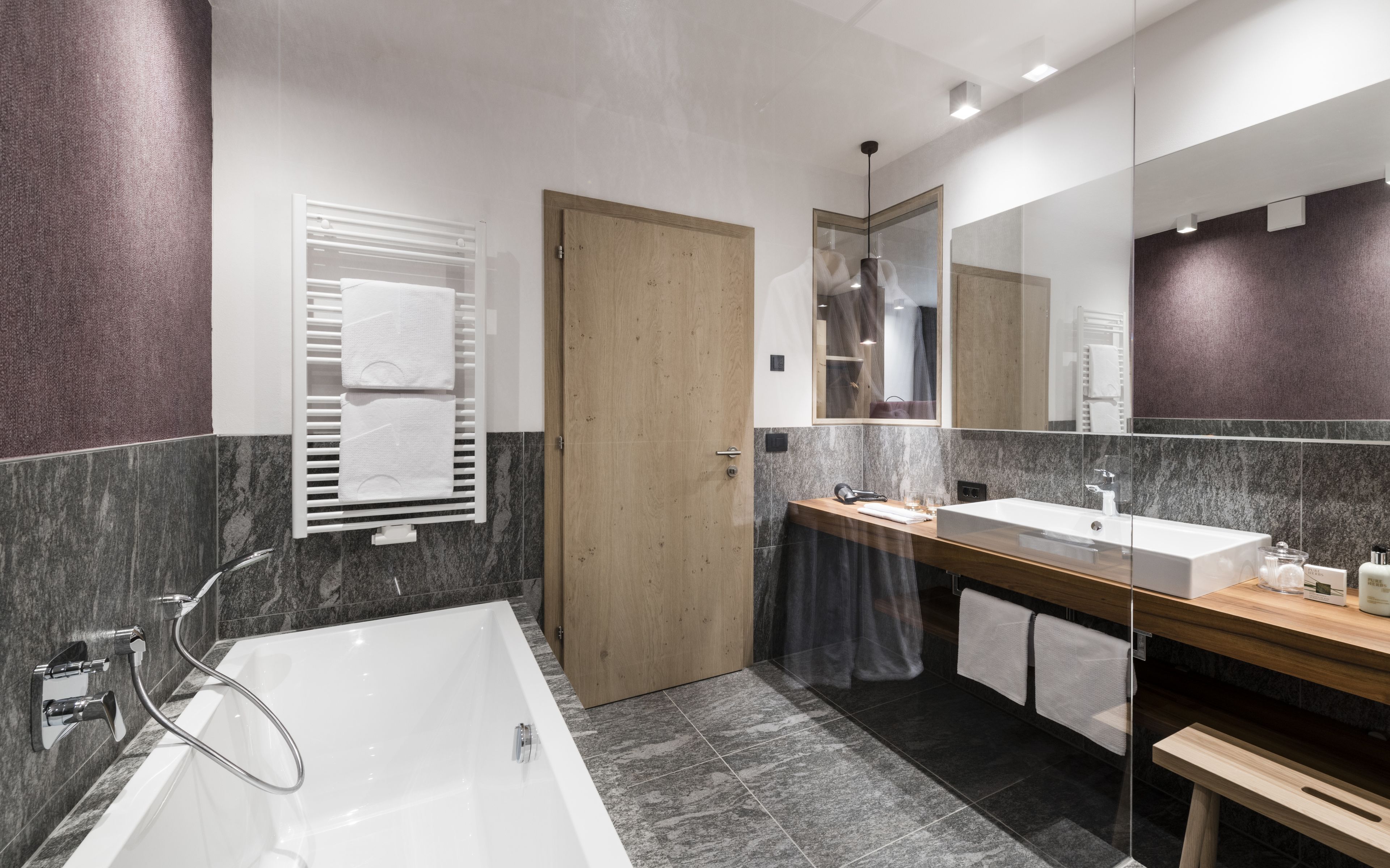 A modern bathroom with a large bathtub, a wooden vanity with a sink, and a mirror.