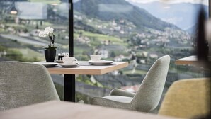 A dining area with a table set for two, a potted plant, and a view of a mountainous landscape. - Vinea - Suites & Apartments (Tirolo)