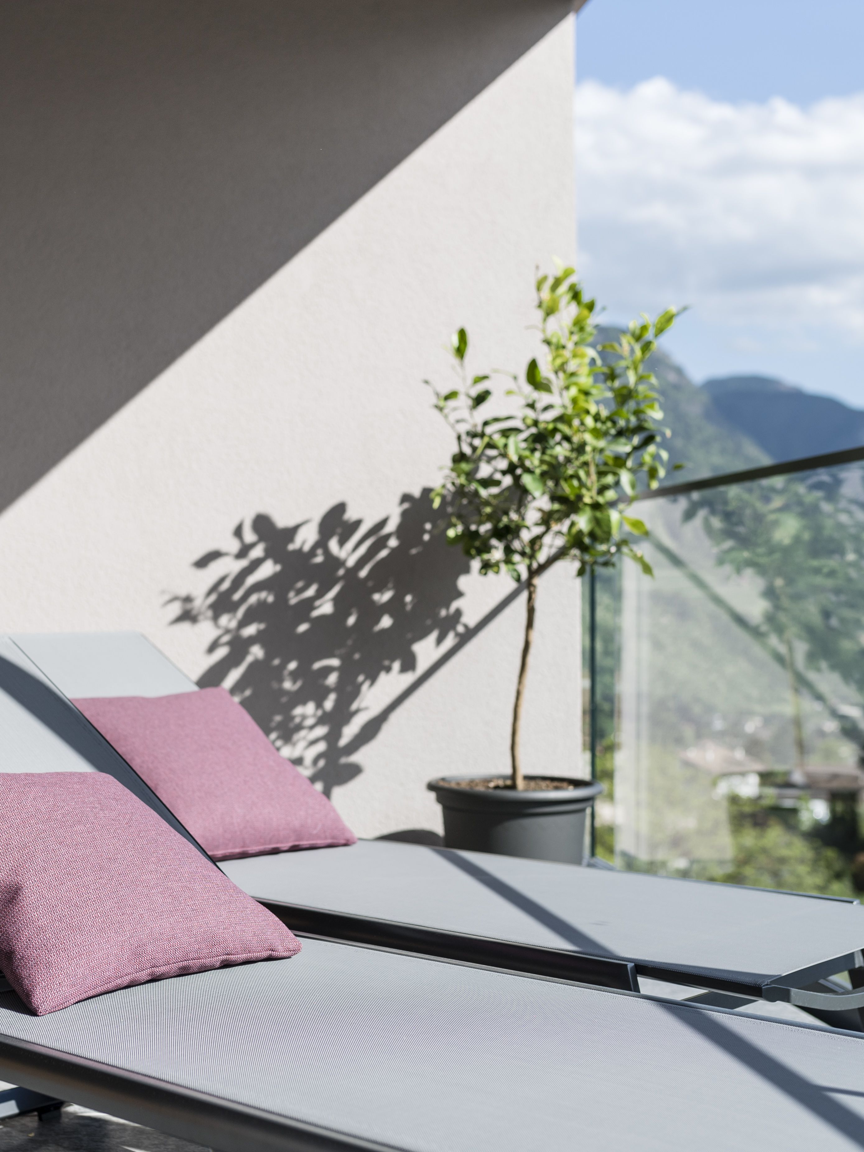 A balcony with a lounge chair, a small potted plant, and a view of mountains.