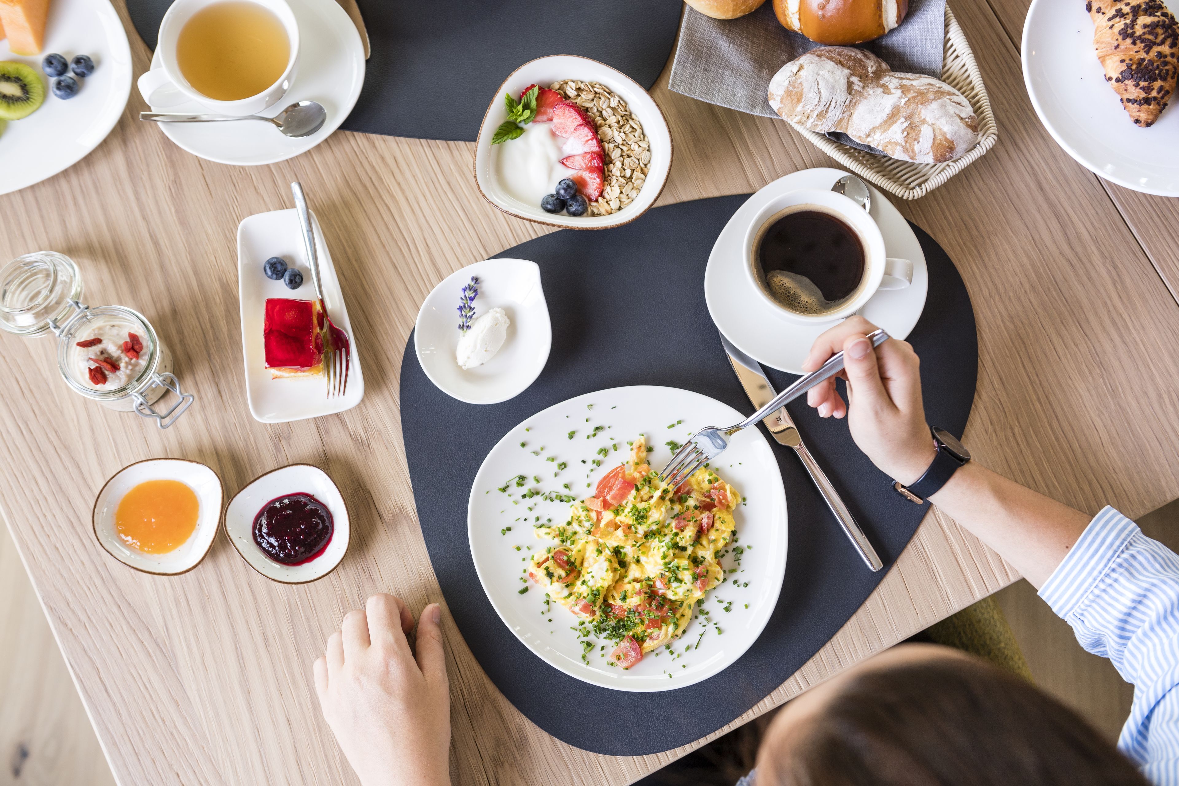 A breakfast setting with various food items and a cup of coffee on a wooden table.