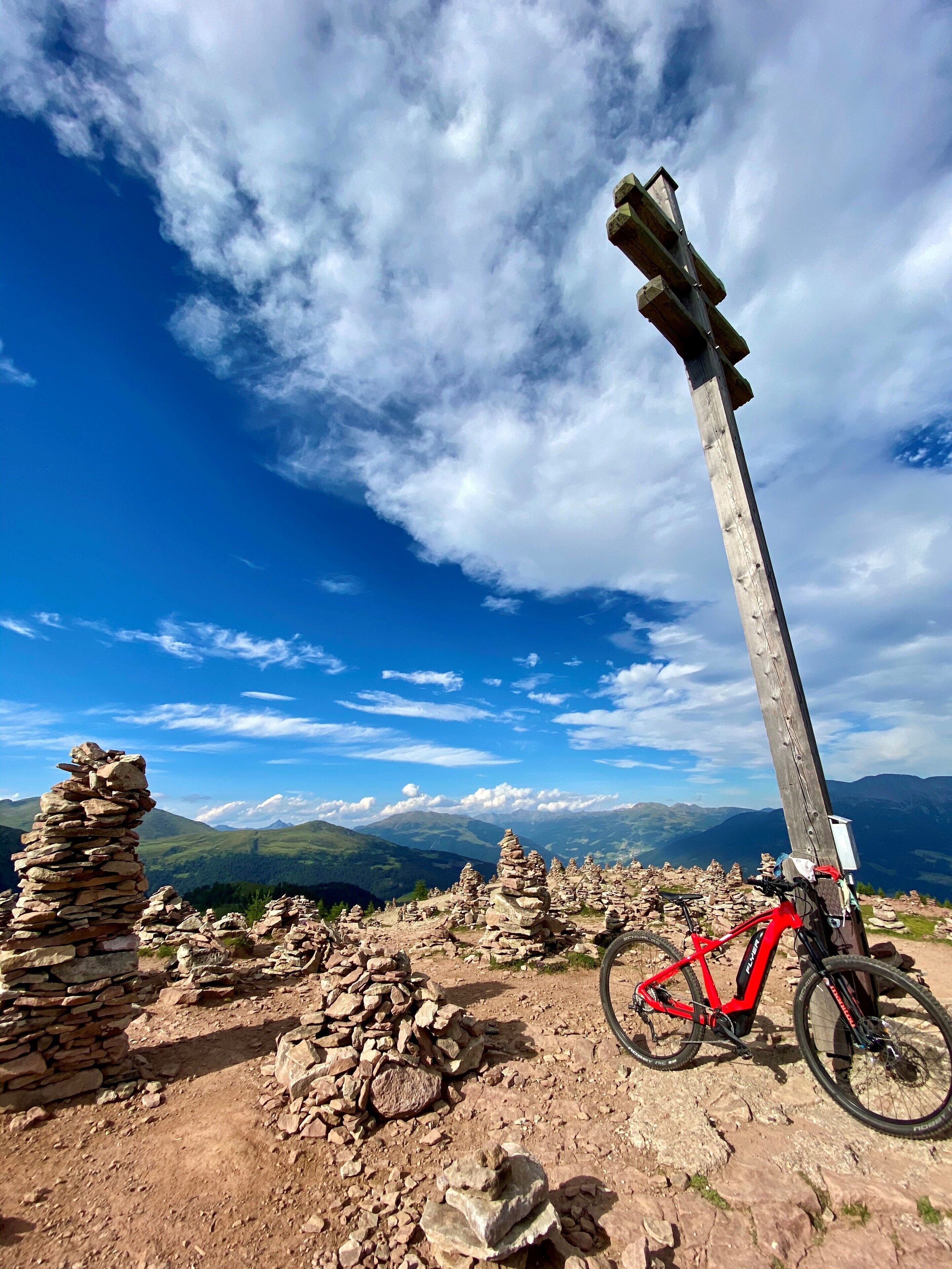 Eine Berglandschaft mit einem hölzernen Kreuz, einem roten Mountainbike und Steinsteinhaufen.