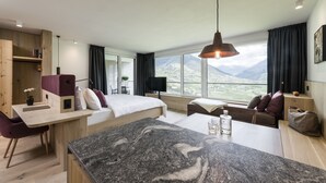 A modern hotel room with a large bed, a desk, and a view of mountains. - Vinea - Suites & Apartments (Tirolo)