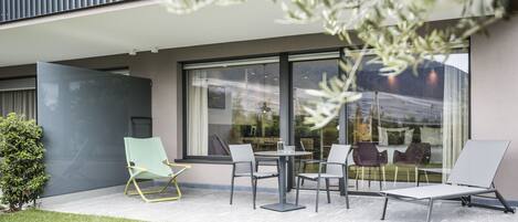 Un área de estar moderna al aire libre con una mesa, sillas, un vidrio y un balcón.