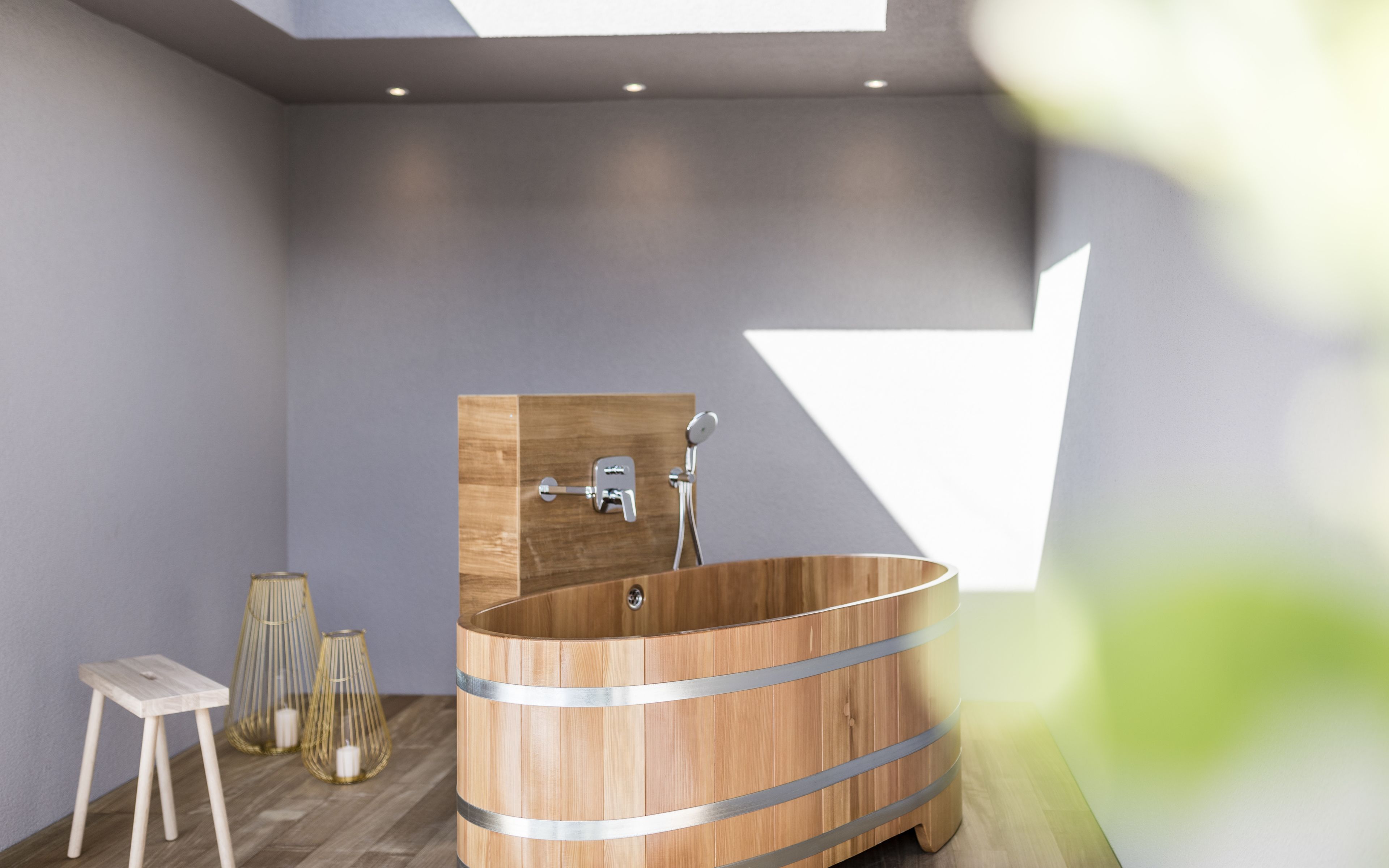 A modern bathroom with a wooden bathtub, a small stool, and decorative glass vases.
