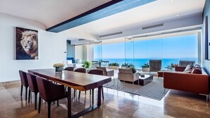 A modern living room with a dining area, large windows, and a view of the ocean.