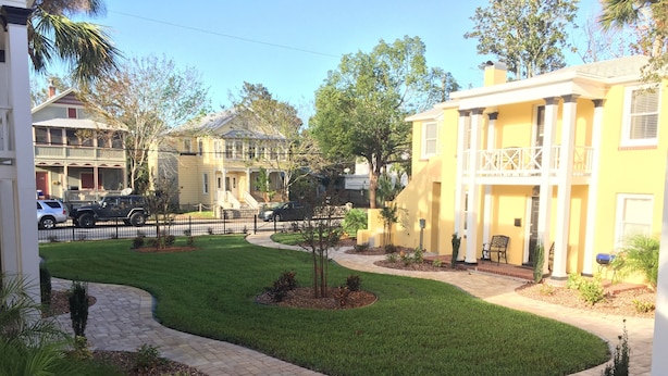 A residential area with a paved walkway, a well-maintained lawn, and a yellow building with a balcony. - C5, Flagler location in downtown, close to beaches, private patio, free parking! (St. Augustine)