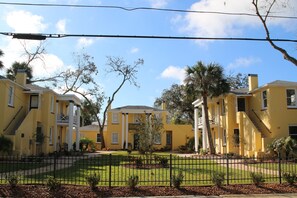 A yellow building with a symmetrical facade, a central entrance, and a well-maintained lawn.