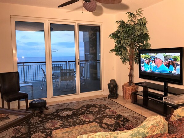 Een woonkamer met een televisie, een plant en uitzicht op de oceaan door grote schuifdeuren.