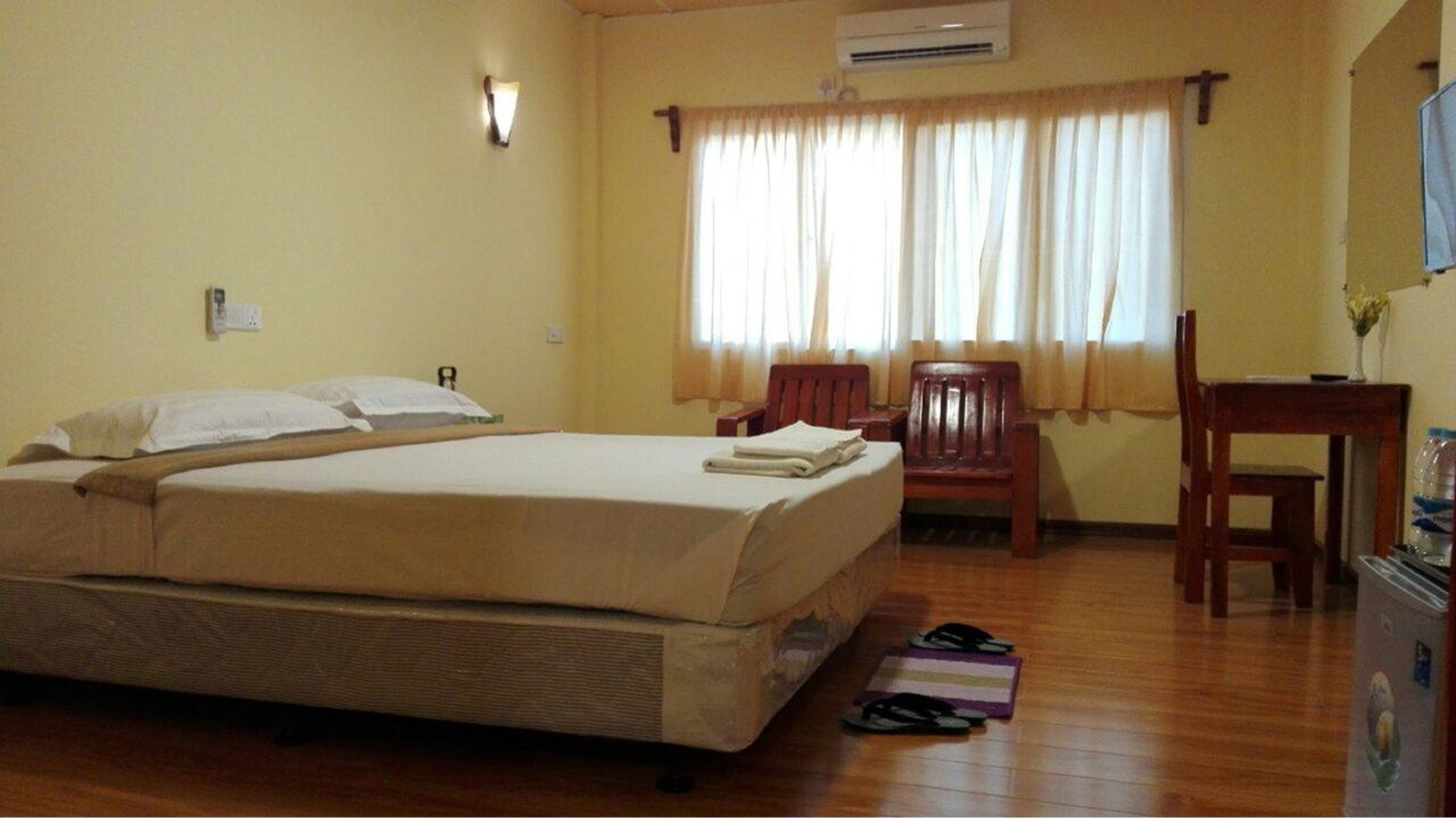 A hotel room with a bed, a chair, a desk, and a window with curtains.