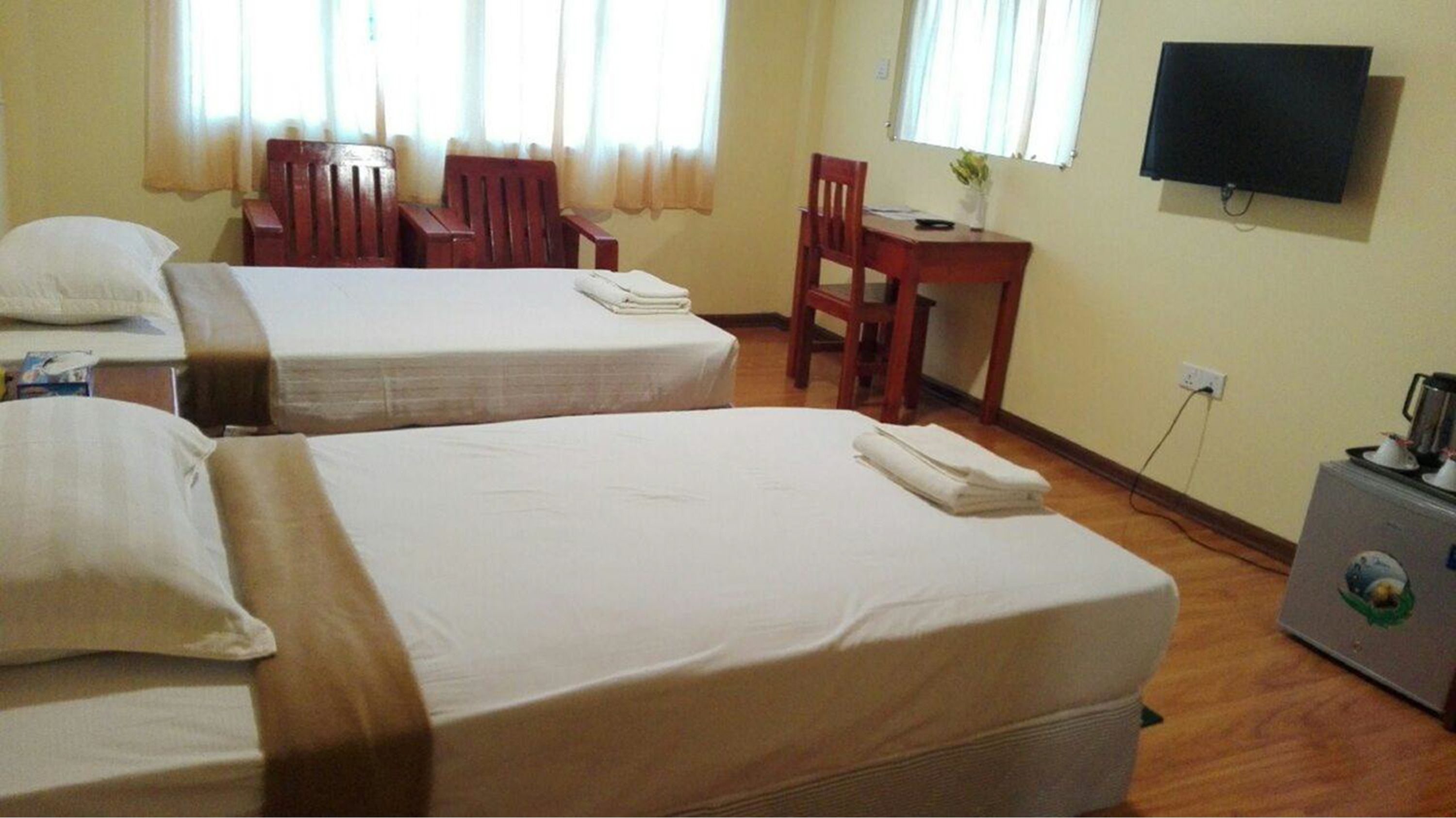Habitación de hotel con dos camas, un escritorio, una silla, un televisor y una kitchenette pequeña.
