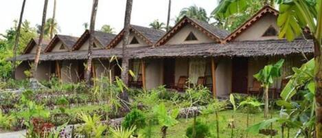 A row of thatched-roof cottages with a lush garden in front.