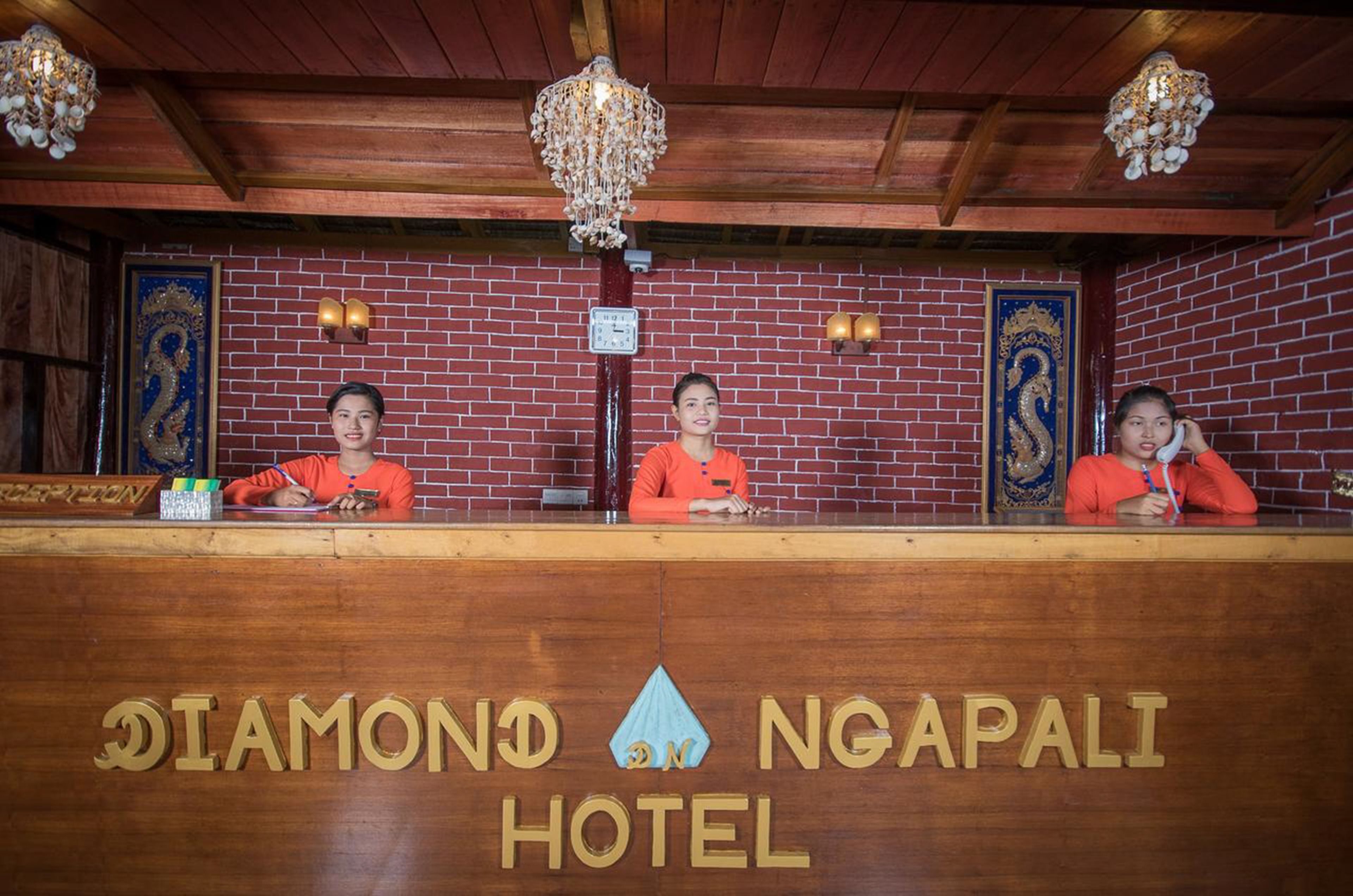 Eine Rezeption des Diamond Ngapali Hotels mit drei Mitarbeitern dahinter.